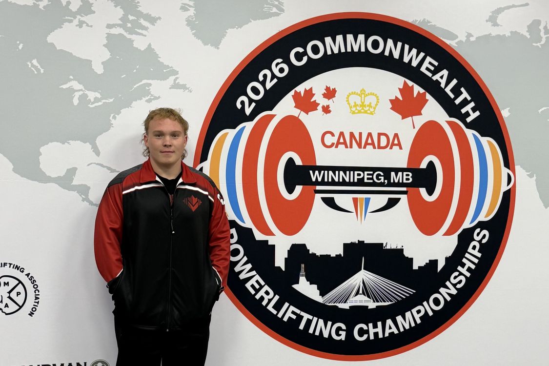 Ty Humphries in front of the logo for the 2026 Commonwealth Powerlifting Championships