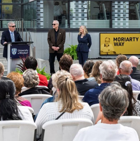 A seated crowd watches a speaker at a podium in front of the Moriarty Way signage at the Toldo Lancer Centre