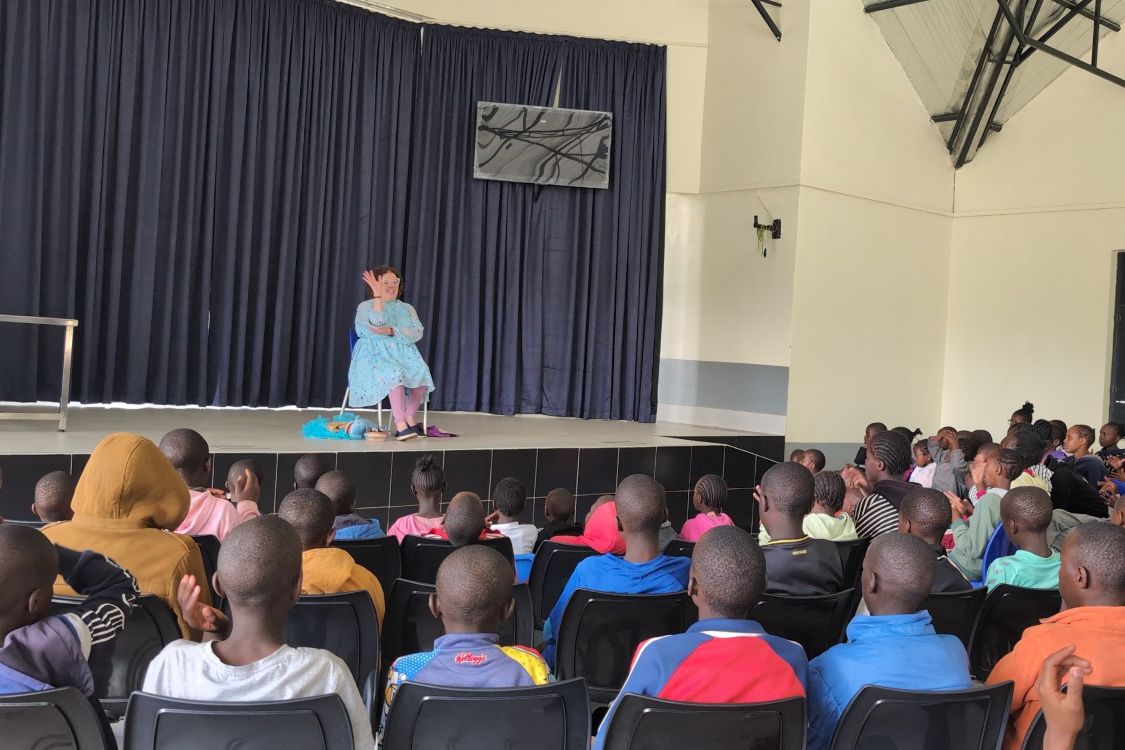 Kate Reynolds leads a storytime from stage in front of Kenyan children