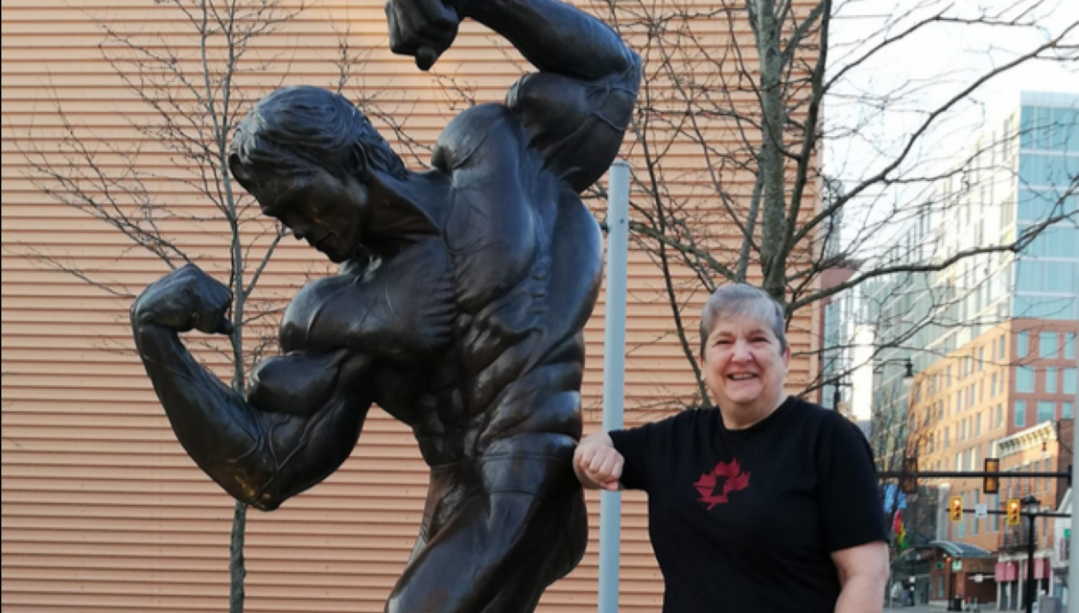Jeanine Watt next to a statue of a bodybuilder