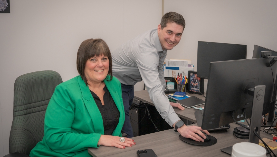 Luke, an mba student stands at the desk of Kim, the Executive he shadowed for the day