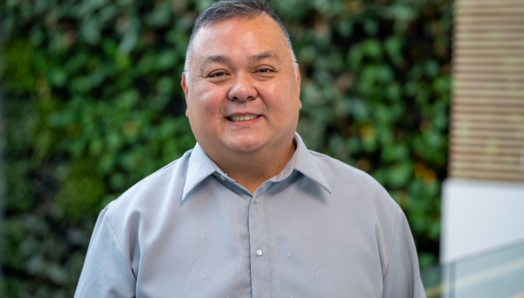 Dr Cruz stands in front of a green wall in the faculty of nursing.