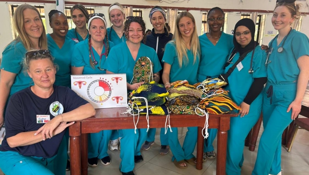 A group of nursing students and faculty stand around a table of menstruation kits in Tanzania.