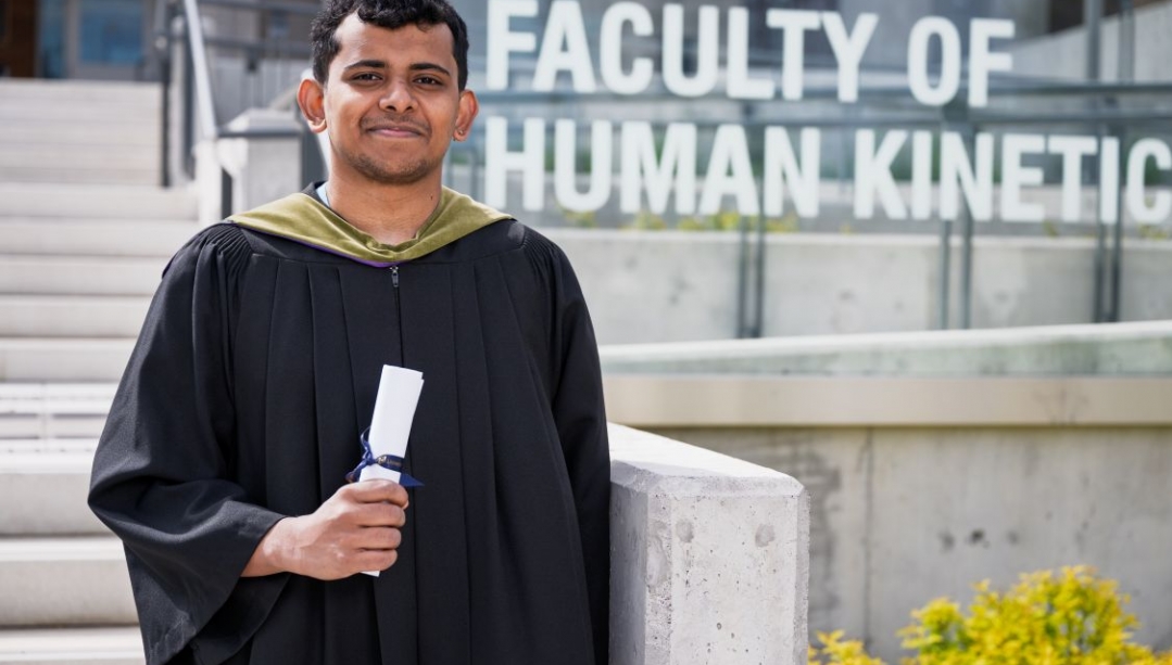 Aravind Manilal Valliyate in grad robe in front of Human Kinetics building
