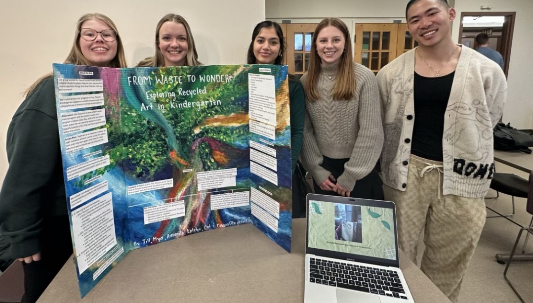Students standing behind a poster board and laptop at the Service Learning Fair