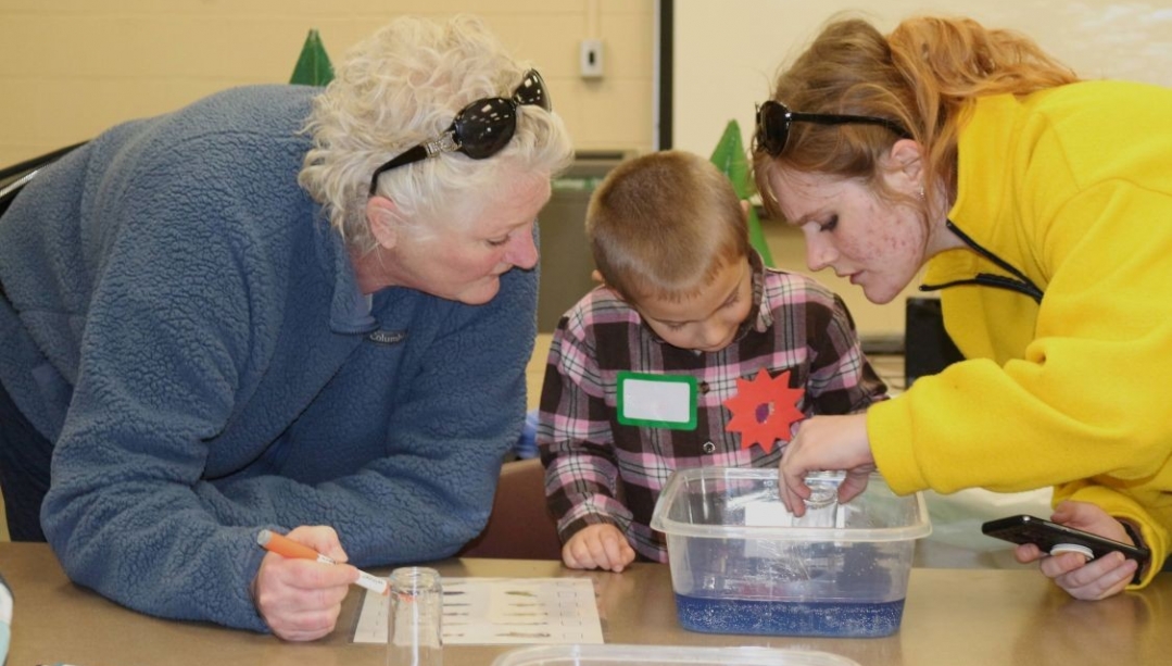 Two women and a young boy are focused on an activity involving a tub of water