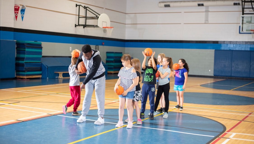 A university student plays a game in a gymnasium with children