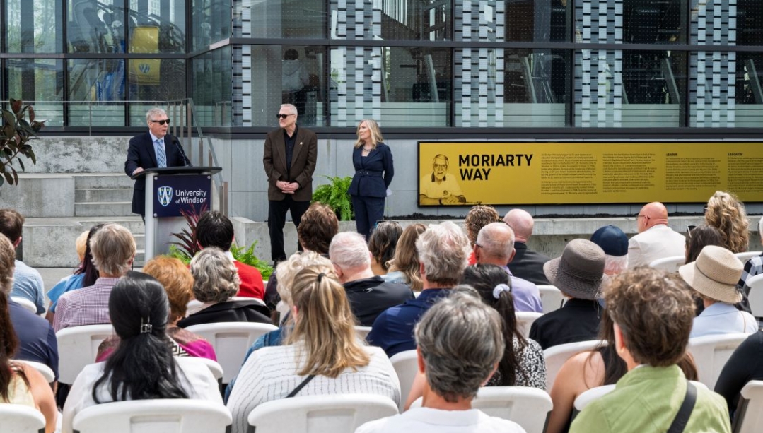 A seated crowd watches a speaker at a podium in front of the Moriarty Way signage at the Toldo Lancer Centre