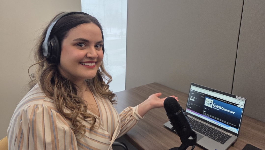 Natasha Nakhle sits at a desk in front of her laptop &amp; microphone.