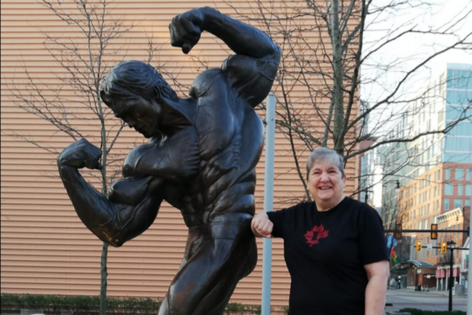 Jeanine Watt next to a statue of a bodybuilder