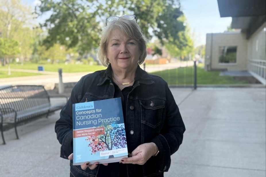 Dean Sheppard-LeMoine stands outside on campus holding the new textbook she co-edited