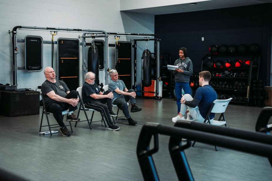three older men do chair stretches across from a UWindsor student with another student observing with a clipboard