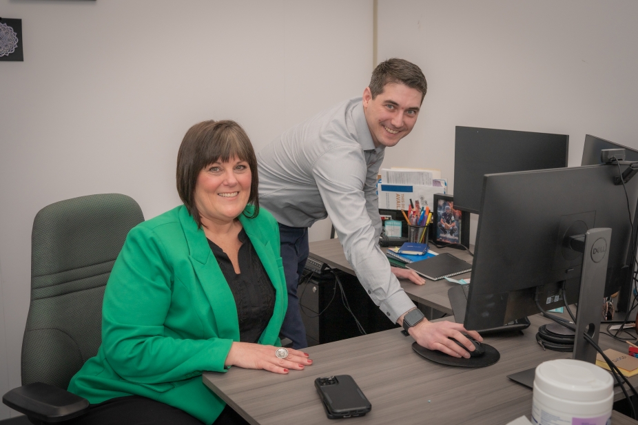 Luke, an mba student stands at the desk of Kim, the Executive he shadowed for the day