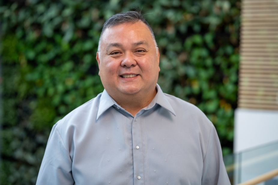 Dr Cruz stands in front of a green wall in the faculty of nursing.