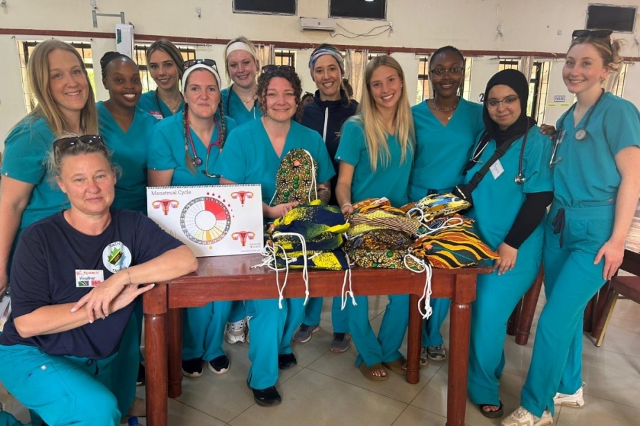 A group of nursing students and faculty stand around a table of menstruation kits in Tanzania.