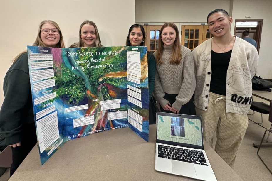 Students standing behind a poster board and laptop at the Service Learning Fair