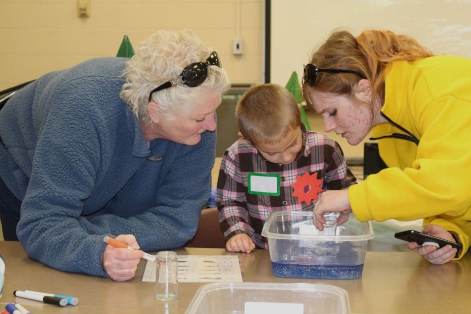 Two women and a young boy are focused on an activity involving a tub of water