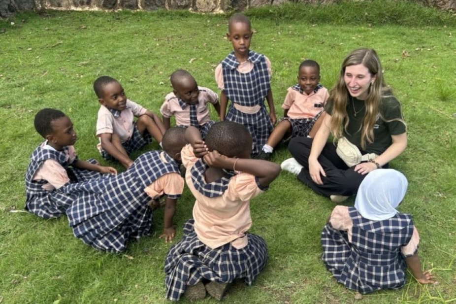 smiling students and a UWindsor teacher candidate sitting in the grass in Tanzania