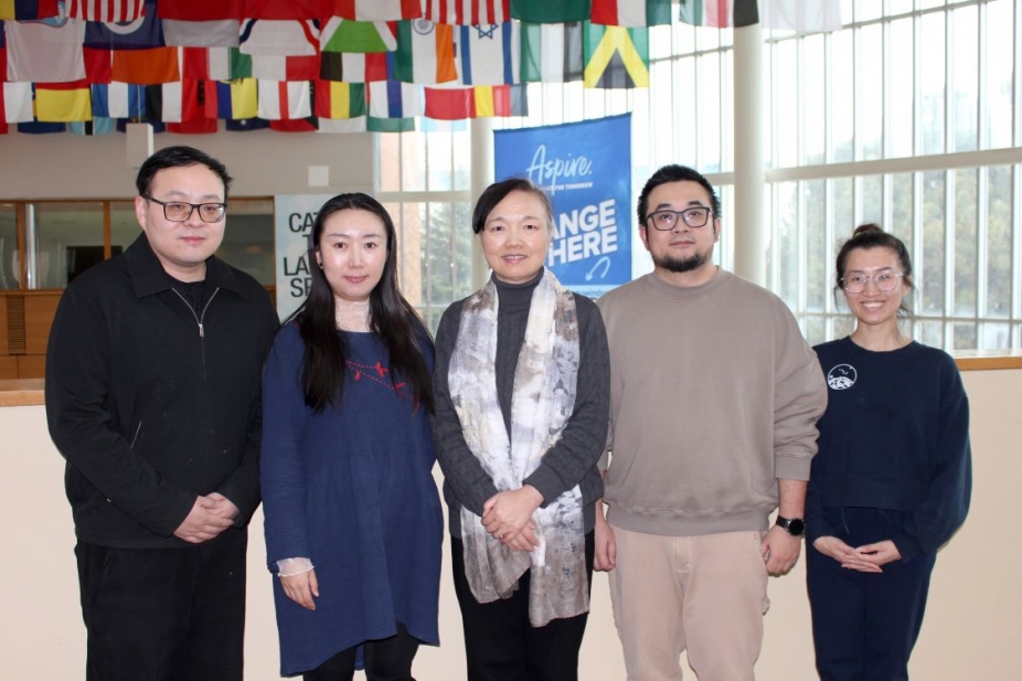 5 people standing in the CAW Student Centre under the flags of many countries with an Aspire banner behind them
