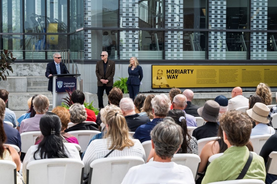 A seated crowd watches a speaker at a podium in front of the Moriarty Way signage at the Toldo Lancer Centre