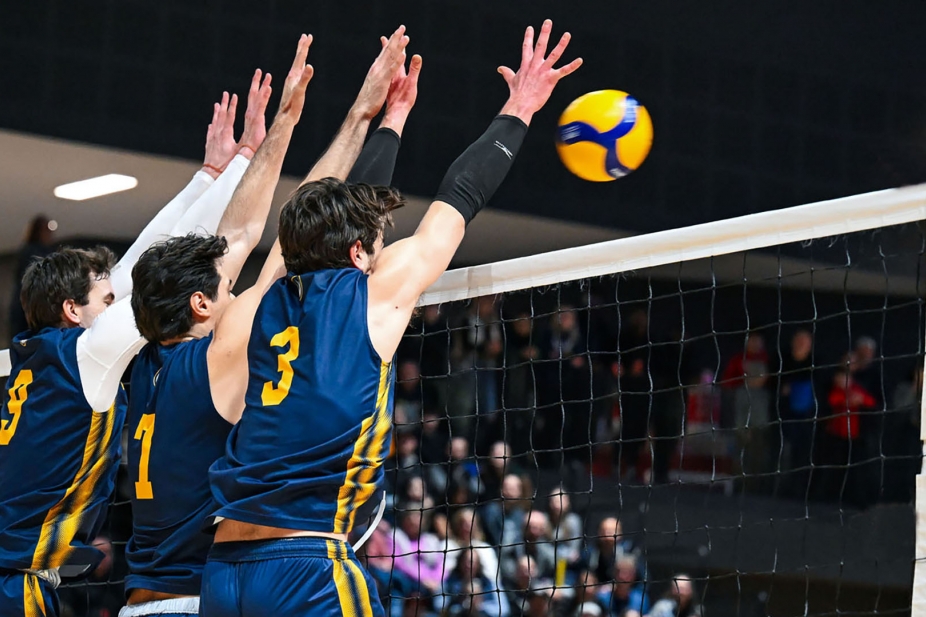 Lancers Men&#039;s Volleyball players jumping at the net for a spike block.