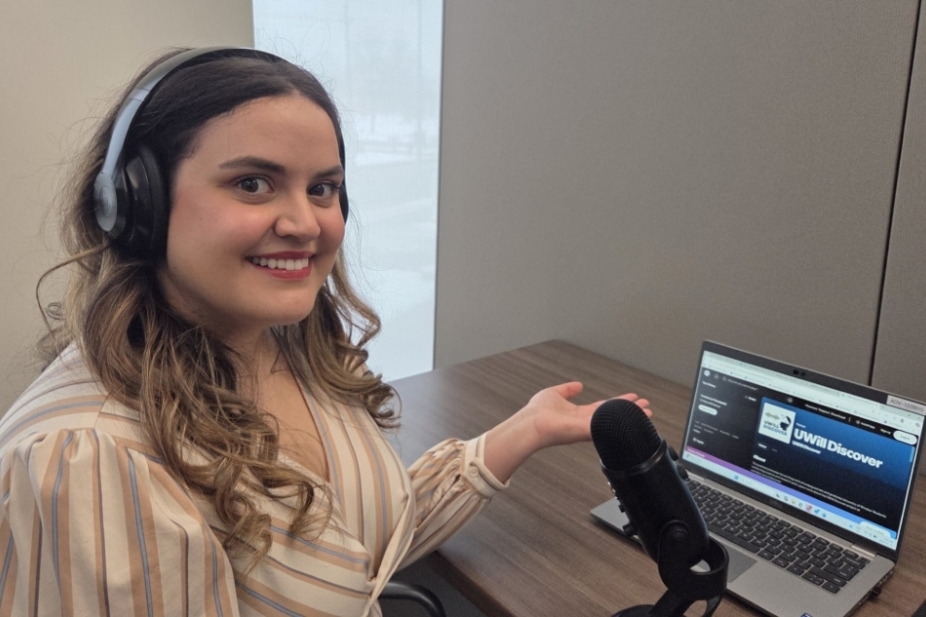 Natasha Nakhle sits at a desk in front of her laptop &amp; microphone.