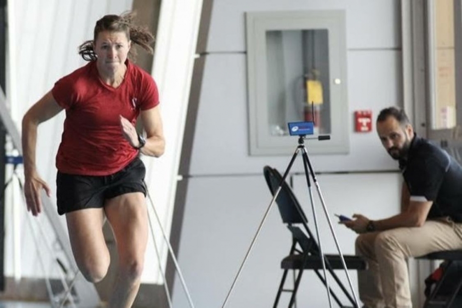 A young woman sprints while a man records information from a chair