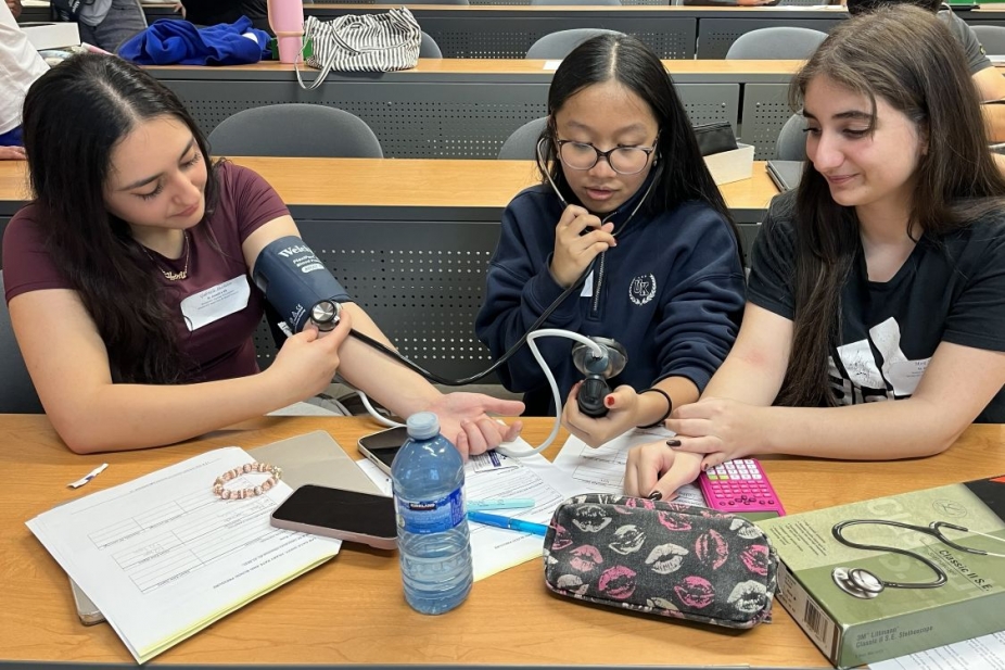 Three high school girls using a blood pressure cuff