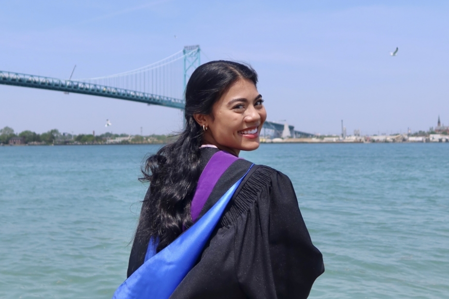 Sara Syed looks over the Detroit River, wearing her graduation robe