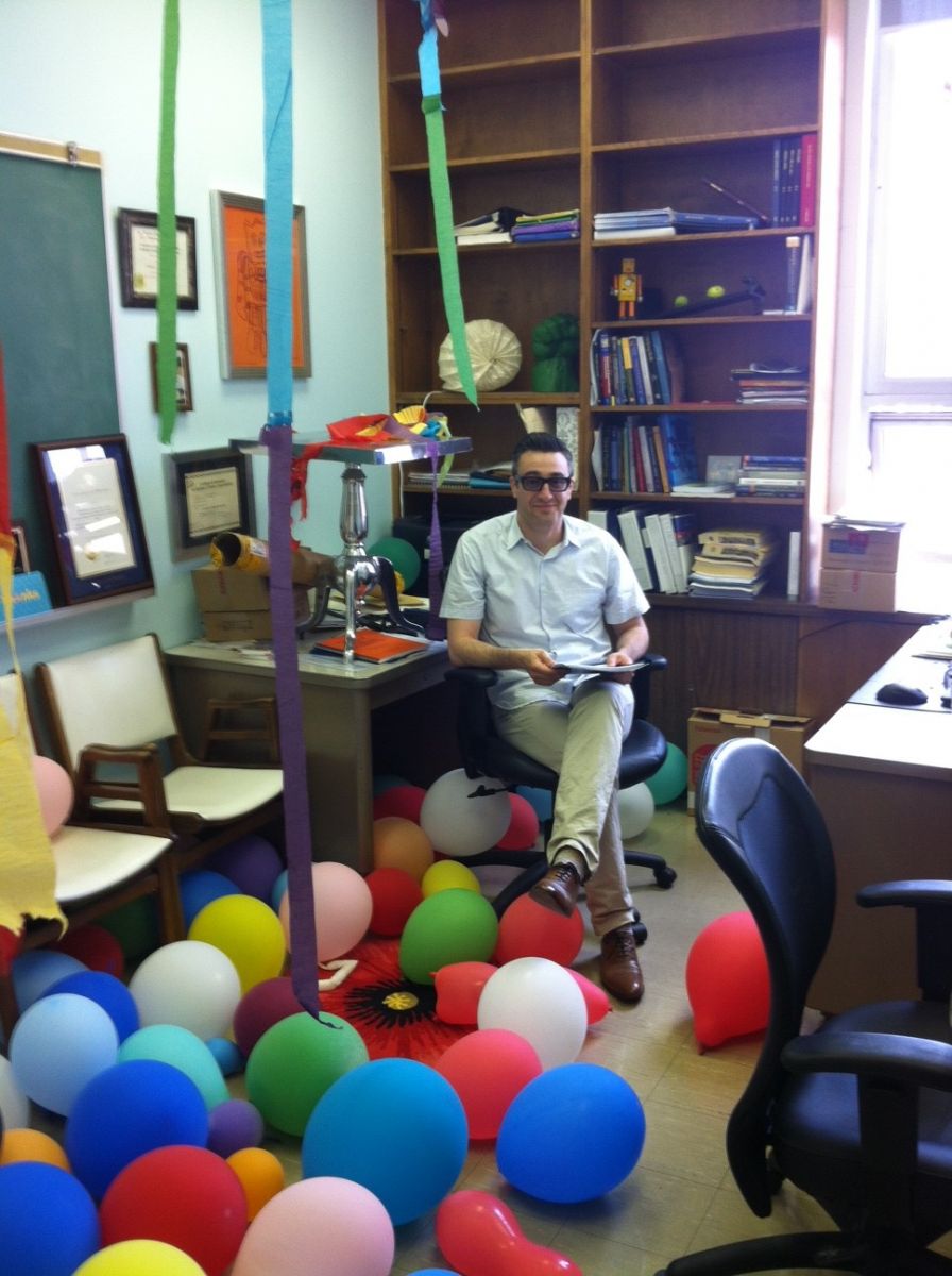 Dr. Pascual-Leone seated in his office, with balloons on the ground and streamers hanging from the ceiling