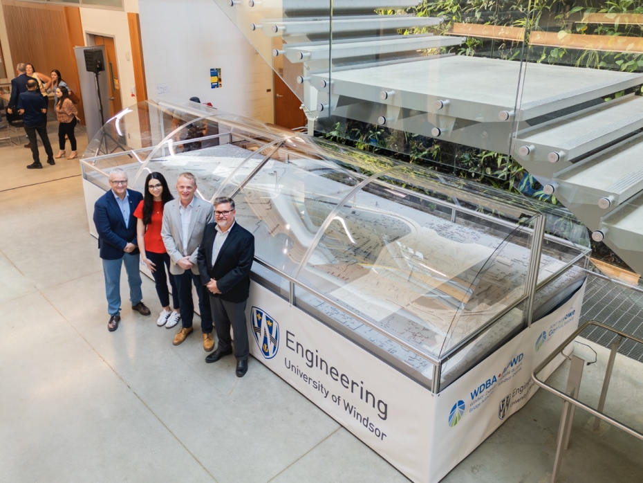 Four people pose in front of a scale model of the Gordie Howe International Bridge