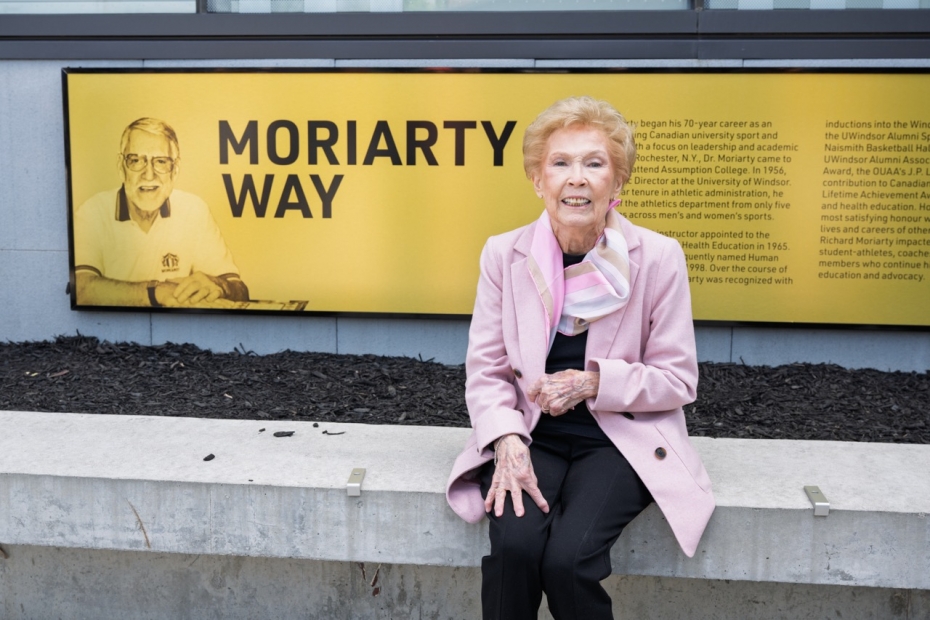 Mary Moriarty sits beside the newly unveiled Moriarty Way sign during a ceremony at the University of Windsor on April 22, 2026, honouring the legacy of her late husband, Dr. Richard Moriarty. (PETER MARVAL/University of Windsor)
