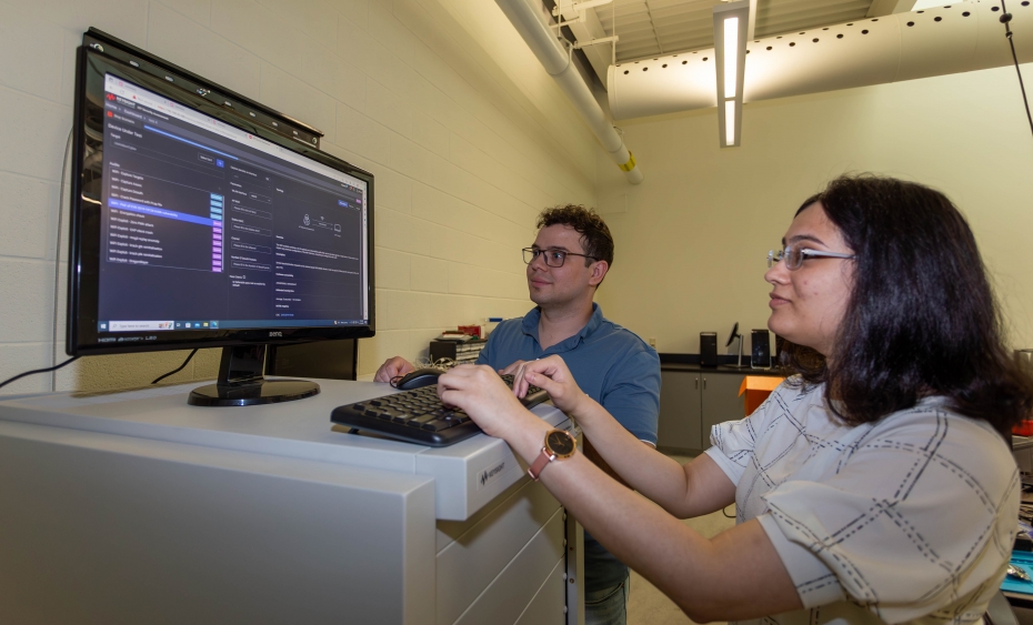 A man and woman look at charts on a computer monitor in a white room.