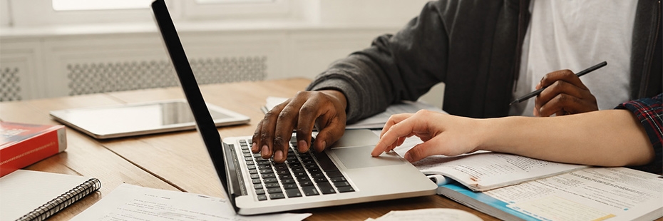 Close distance image of students' hands on laptop keyboard with books all around