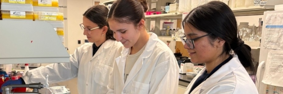 Three students in lab coats working at a research lab bench