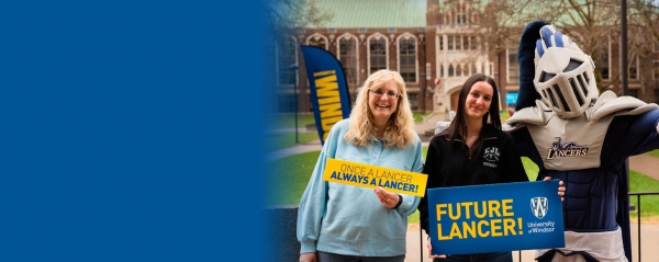Lancer mascot with two women holding UWindsor Lancer signs. Dillon Hall in background.