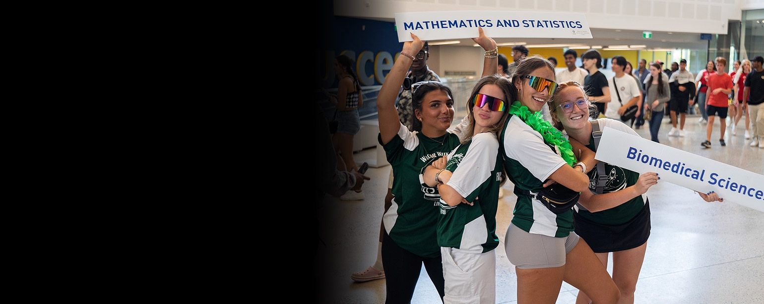 Four students posing and smiling holding program signs