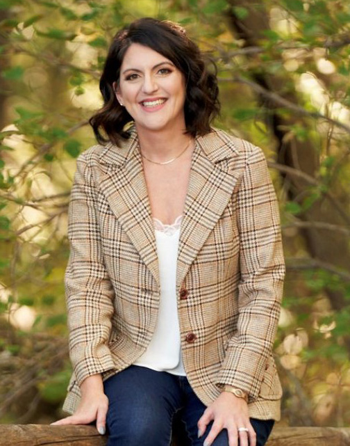 Woman sitting in a wooden setting, on a tree branch, smiling.