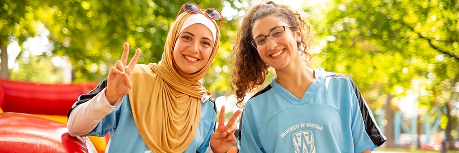 Two female smiling in front of a fun inflatable slide while at Welcome Week