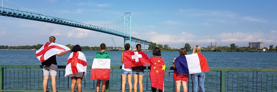 Incoming exchange students posing with their flags in front of the Ambassador bridge