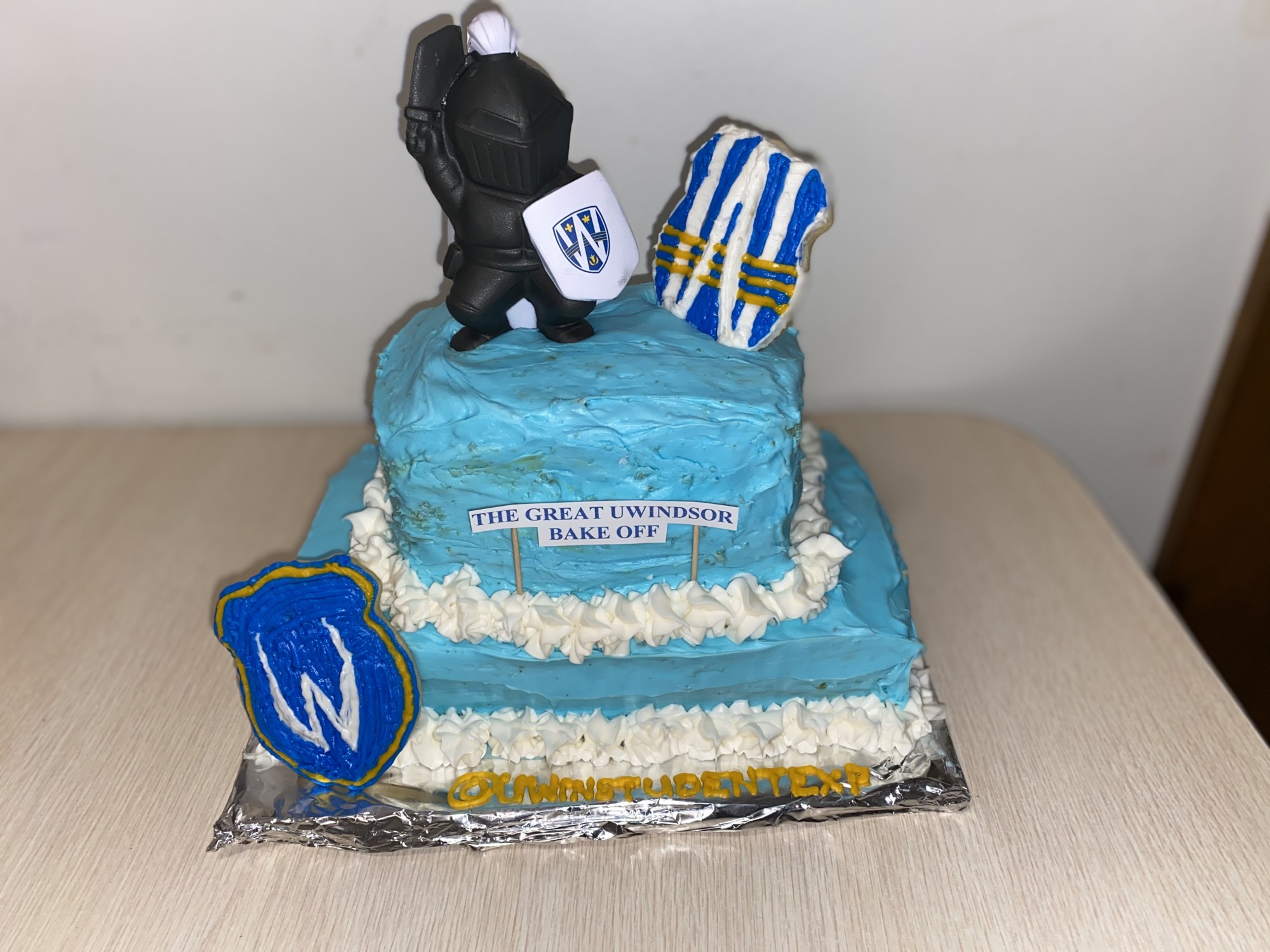 A blue and gold cake with a lancer holding the university of Windsor sheild
