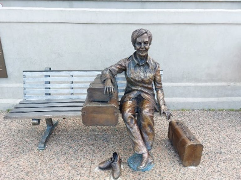 A statue of a luggage and a person sitting on a bench