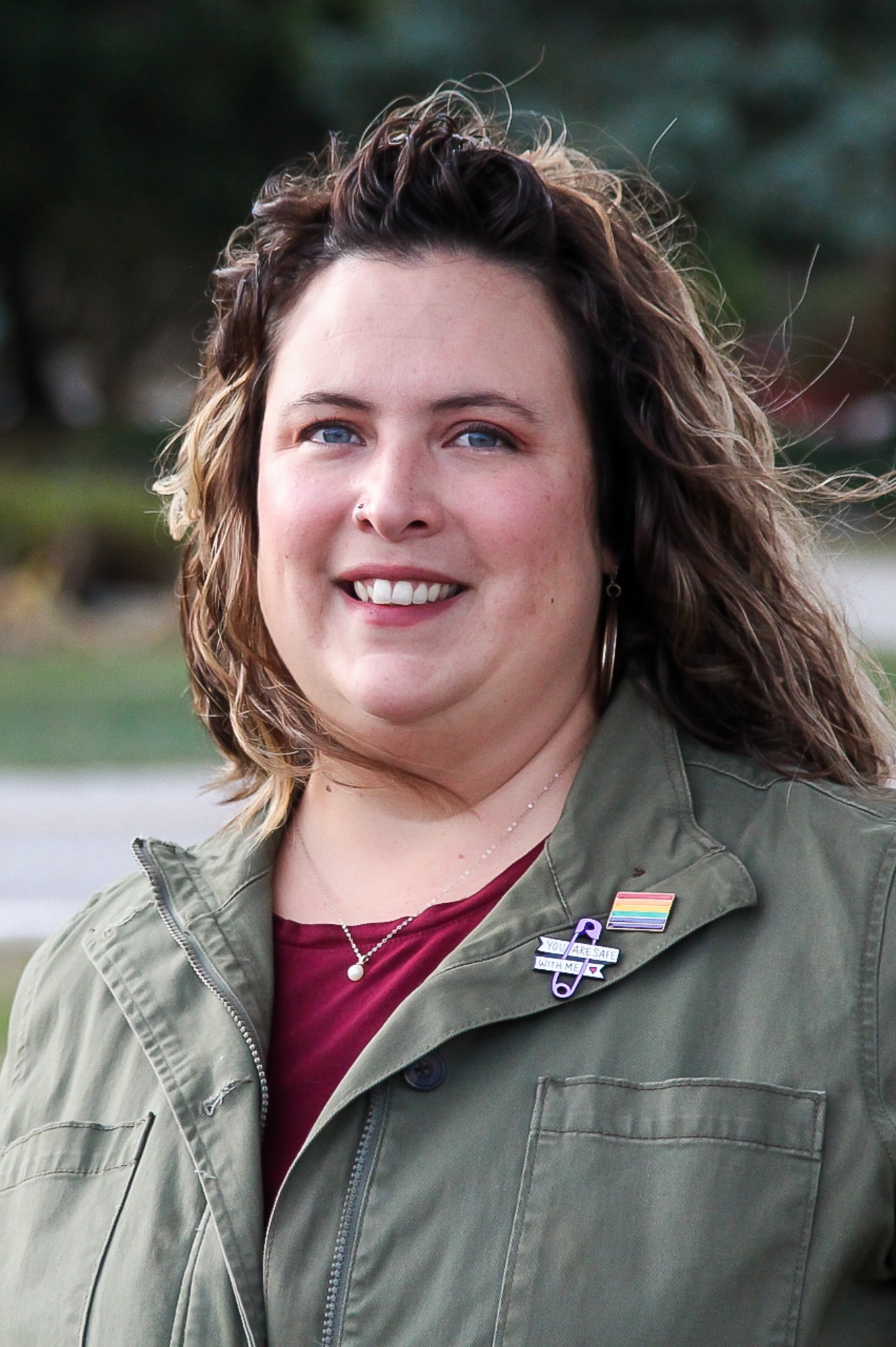 Pride Committee co-chair Joyceln Lorito smiles at camera with pride pins on her jacket