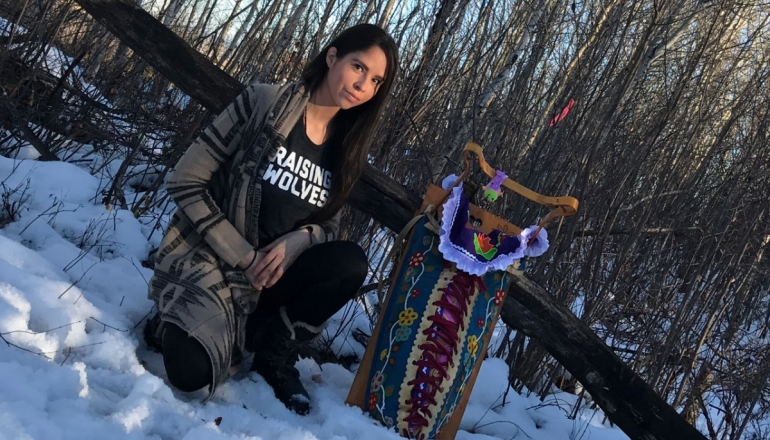 Andrea Landry is shown in a snowy, wooded area, with her baby, both in traditional Aboriginal attire.