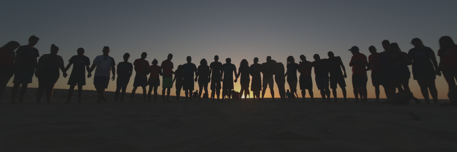 Silhouette of young adults standing together in front of a sunrise facing away from the camera